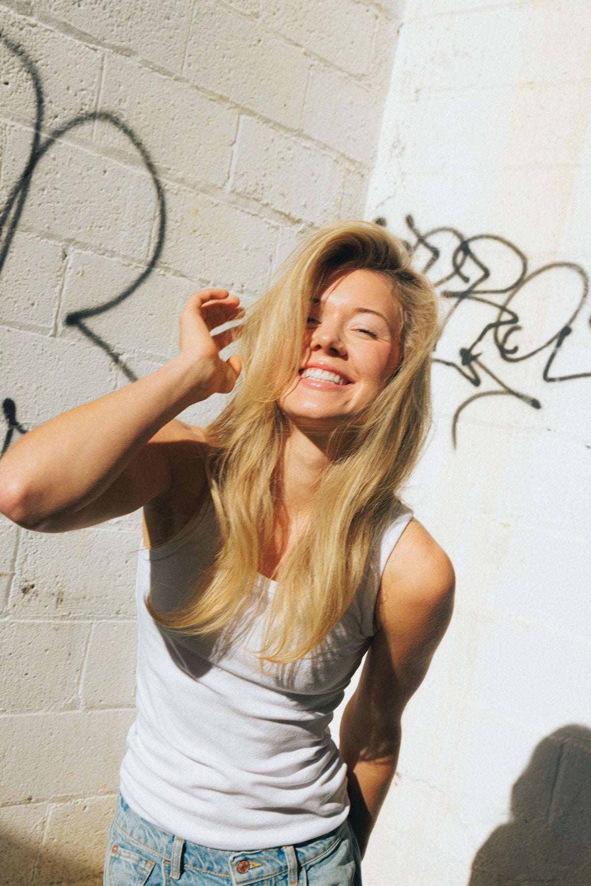 Lachende vrouw met lang blond haar in de zon voor een witte muur