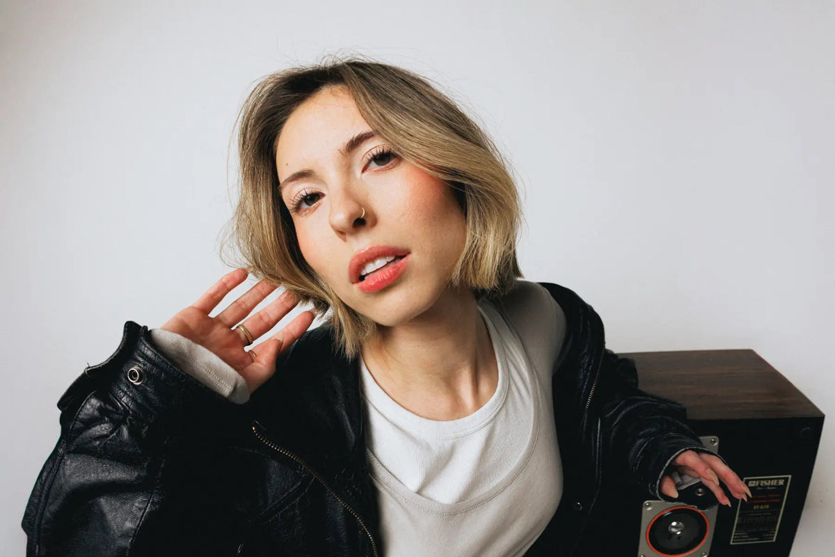 Vrouw met een blonde bob in een leren jack leunt op een luidspreker