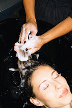 Shampoo wordt tot schuim gemasseerd in het haar van een vrouw aan de wasbak