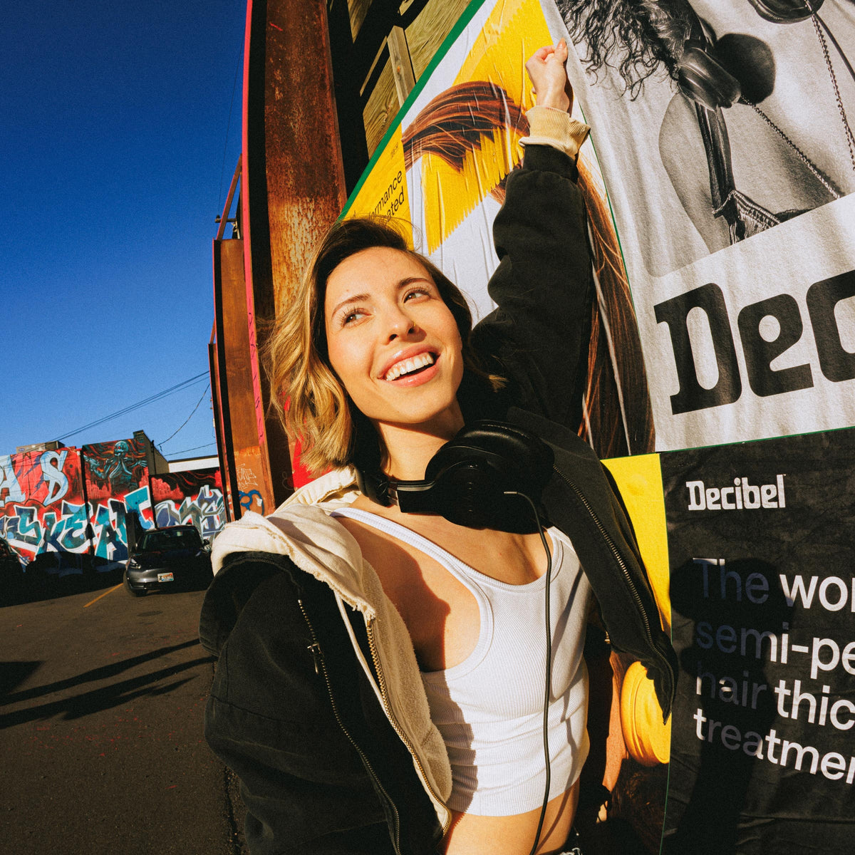 Lachende vrouw met een koptelefoon om haar nek naast een Decibel poster op straat