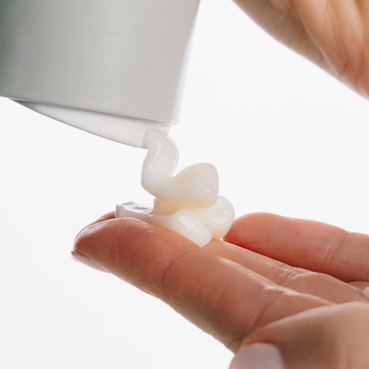 Witte crème wordt uit een tube op een vingertop geknepen
